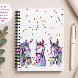 May include: A spiral-bound notebook featuring a white cover with a colourful watercolour illustration of three horses and scattered small hearts. The text on the cover reads: Can be personalised & choice of lined and plain paper.