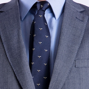 May include: A dark blue suit jacket with a light blue shirt and a dark blue tie featuring a pattern of yellow bees.