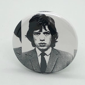 Puede incluir: Botón de foto en blanco y negro con un hombre con traje y corbata. El hombre tiene el pelo corto y oscuro y mira directamente a la cámara.