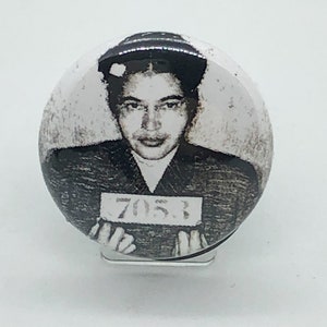 Puede incluir: Botón en blanco y negro con una foto de Rosa Parks, una activista por los derechos civiles, con el número 7051 impreso en un cartel.