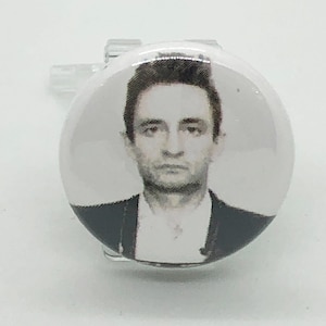 Puede incluir: Una foto en blanco y negro de un hombre con el pelo oscuro, que lleva una chaqueta de traje. La foto está impresa en un botón blanco.