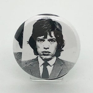 Puede incluir: Un botón en blanco y negro con un retrato de un hombre con traje y corbata. La imagen es un primer plano del rostro del hombre, con cabello oscuro y una expresión seria. El botón es redondo y tiene un acabado brillante.