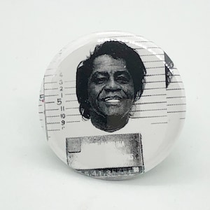 Puede incluir: Foto en blanco y negro estilo ficha policial de una mujer con cabello negro corto. La foto está sobre un fondo blanco con un patrón de cuadrícula en blanco y negro.