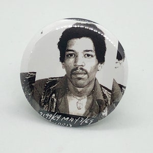 Puede incluir: Foto en blanco y negro de Jimi Hendrix en un botón. El botón tiene el texto "219924 MAY 3169" escrito en él.