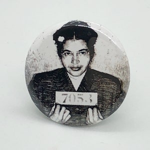 Puede incluir: Foto en blanco y negro de una joven con el pelo corto, vistiendo una camisa con cuello y sosteniendo un cartel que dice "705.3".