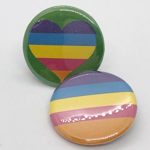 May include: Two round button pins with a rainbow pride flag design. One pin features a heart-shaped rainbow flag and the other pin features horizontal rainbow stripes.
