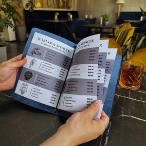 Puede incluir: Un men&uacute; azul y blanco para el restaurante de mariscos Warner & Spencer. El men&uacute; enumera varios platos de mariscos con precios. El men&uacute; est&aacute; abierto a una p&aacute;gina con el encabezado "Oyster Spicy Curry" y un precio de 24,00 &euro;.