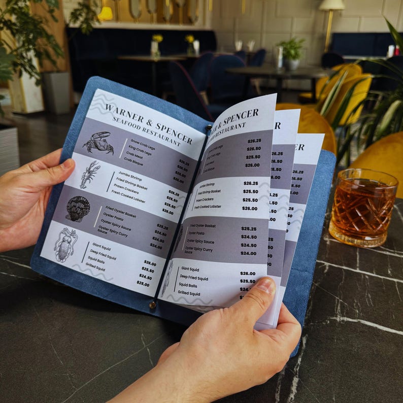 Puede incluir: Un men&uacute; azul y blanco para el restaurante de mariscos Warner & Spencer. El men&uacute; enumera varios platos de mariscos con precios. El men&uacute; est&aacute; abierto a una p&aacute;gina con el encabezado "Oyster Spicy Curry" y un precio de 24,00 &euro;.