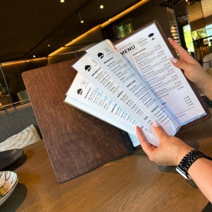 May include: A wooden menu holder with a dark brown finish, displaying menu pages with text. The menu pages are held in clear plastic sleeves. The menu includes breakfast, appetizer, main course, and dessert options.