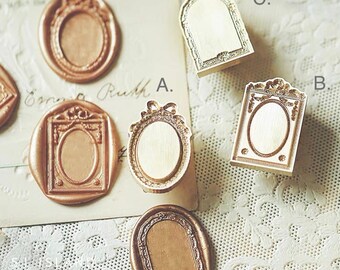 May include: Set of six gold-toned metal wax seal stamps with different ornate designs. Each stamp features a frame with a blank oval or rectangular space in the centre. The stamps are labelled A, B, and C.