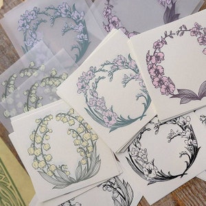 May include: A stack of cards featuring floral designs. The cards depict various floral patterns, including lilies of the valley, freesia, and orchids. The cards are printed on cream-coloured paper.