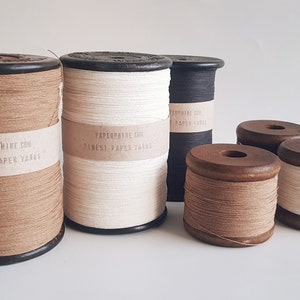 May include: Five spools of paper yarn in various colors, including brown, white, and black. The spools are made of wood and have labels that read "PAPERPHINE.COM FINEST PAPER YARNS".