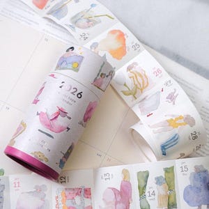 Könnte beinhalten: Eine Rolle 2026 Washi-Tape-Kalender mit Aquarellillustrationen von Personen und Objekten. Das Band ist abgerollt und zeigt Kalenderdaten und weitere Illustrationen. Die Rolle hat eine rosa Basis.