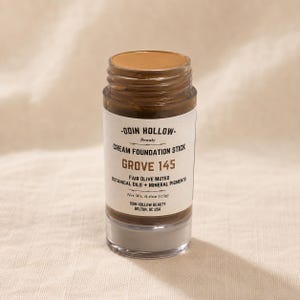 May include: A cream foundation stick by Odin Hollow. The product is labelled "GROVE 145" and contains botanical oils and mineral pigments. The stick is fair olive muted and weighs 17g. The product is in a clear container with a brown cap.