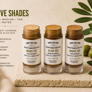 May include: Three cream foundation sticks in clear glass containers with brown lids. The labels read Moss 115, Olive 125, and Grove 145, for fair, medium, and tan olive skin. The text on the label includes "Botanical Oils" and "Creamy Blend".