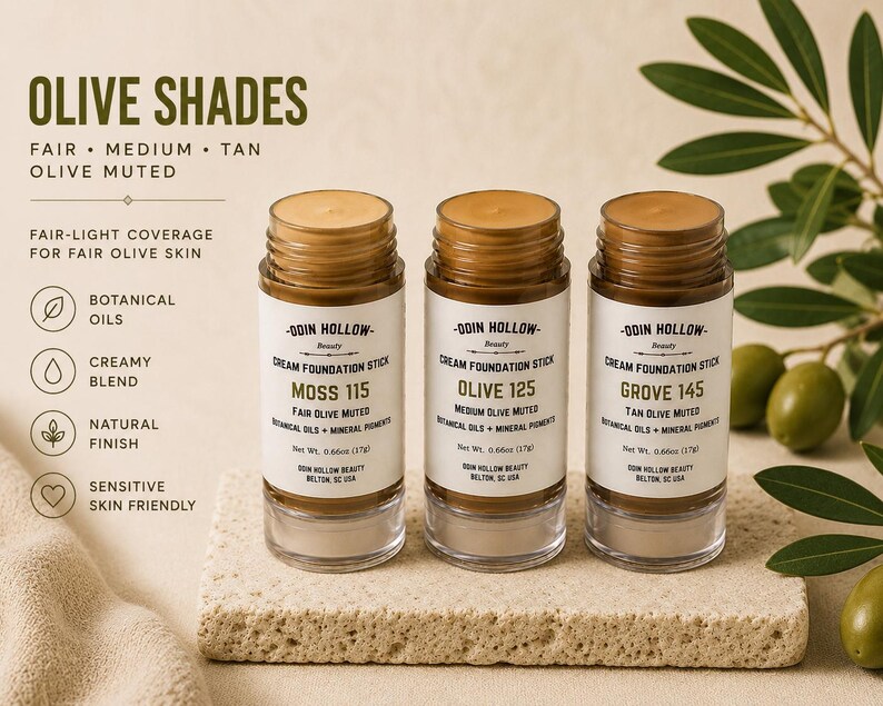 May include: Three cream foundation sticks in clear glass containers with brown lids. The labels read Moss 115, Olive 125, and Grove 145, for fair, medium, and tan olive skin. The text on the label includes "Botanical Oils" and "Creamy Blend".