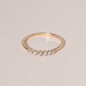 May include: A delicate gold ring featuring a series of small, sparkling gemstones set in a row. The ring has a thin band and a minimalist design, perfect for everyday wear. The gemstones are evenly spaced and catch the light, adding a touch of elegance.