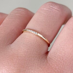 May include: A delicate gold band ring with a row of small diamonds set in the center.