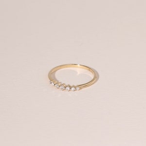May include: A delicate gold ring featuring a series of small, sparkling diamonds set in a row. The ring has a thin band and a polished, reflective surface. The diamonds are evenly spaced and add a touch of elegance.