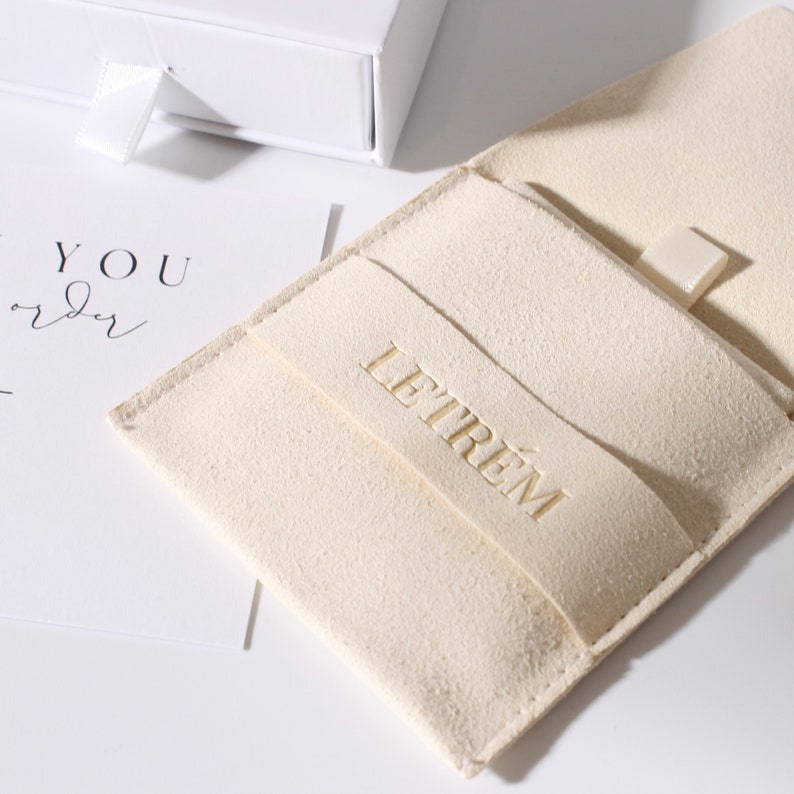 May include: A close-up of a cream-colored suede jewelry pouch with the embossed brand name "LETREM". A white gift box with a ribbon and a card with the words "YOU order" are also visible.