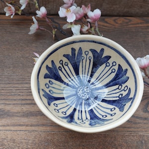 May include: A white ceramic bowl with a blue floral design. The bowl has a white background with a blue floral pattern in the center. The bowl is on a wooden surface.