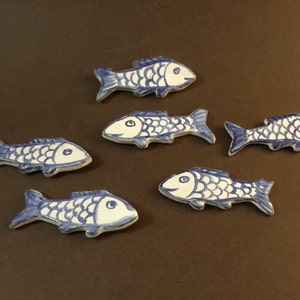 May include: Six ceramic fish figurines in a blue and white color scheme. The fish are all facing the same direction and have a simple, stylized design.