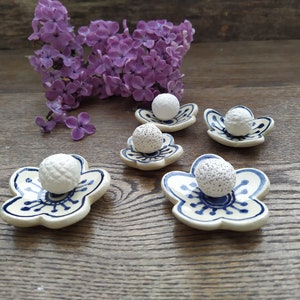 Può includere: Cinque piatti in ceramica bianca a forma di fiore con disegni blu e bianchi, ognuno con una palla bianca con superficie testurizzata.