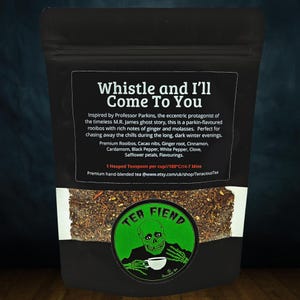 May include: A black bag of loose leaf tea with the text "Whistle and I'll Come To You". The bag features a green circular logo with a skull and the words "Tea Fiend". The tea blend includes rooibos, cacao nibs, ginger root, and other spices.