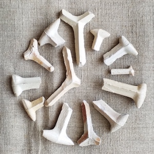 以下が含まれることがあります： ベージュの布地に、13個の白いセラミック製の靴修理用具が円形に並べられています。さまざまな形とサイズがあります。