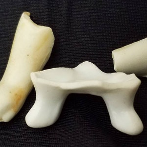 May include: Three broken porcelain doll parts: a leg, an arm, and a torso. The pieces are white with some discoloration.