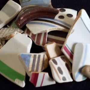 May include: A pile of broken white ceramic plates with various colorful patterns, including red, blue, green, and black.