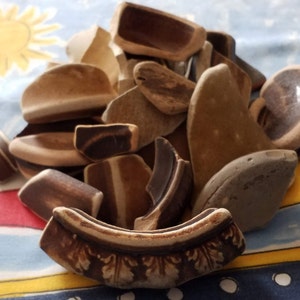 May include: A pile of broken pottery shards in various shades of brown and gray. The shards are arranged in a random pattern, with some overlapping others. The shards are all different sizes and shapes, and some have intricate designs.