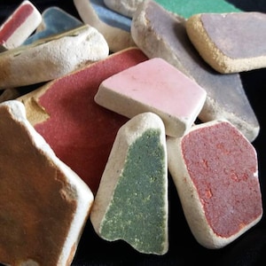 May include: A collection of colorful, irregularly shaped ceramic tiles with various shades of red, green, pink, brown, and purple. The tiles have a rough, textured surface and appear to be handmade.