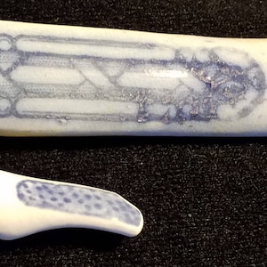 May include: Two pieces of broken blue and white ceramic with a geometric pattern. The larger piece is rectangular and the smaller piece is curved.