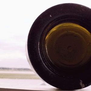 May include: Close-up of the bottom of a glass bottle with a black metal cap. The cap has a gold-colored interior.