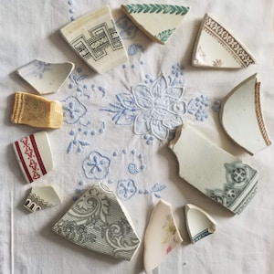 May include: A collection of vintage ceramic plates with floral and geometric patterns in shades of white, green, and red. The plates are broken into various shapes and sizes, suggesting they are fragments.