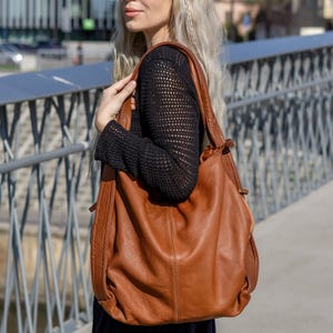 May include: A large, slouchy hobo-style shoulder bag crafted from textured brown leather. The bag features a spacious main compartment, vertical stitched detailing on the front panel, and a wide, integrated shoulder strap for comfortable carrying.