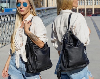 May include: A black leather backpack with a textured surface, featuring a large front zipped pocket and adjustable straps. The bag is shown from both a front-facing perspective and a back-facing perspective, highlighting its versatile design.