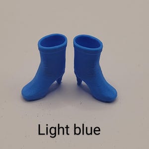 Puede incluir: Un par de botines azul claro con tacones peque&ntilde;os. Los botines tienen una punta redondeada y una superficie texturizada. El texto "Light blue" se muestra debajo.
