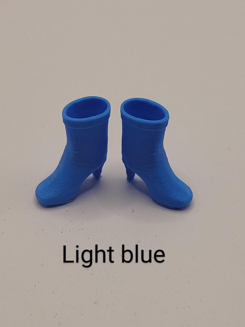 Puede incluir: Un par de botines azul claro con tacones peque&ntilde;os. Los botines tienen una punta redondeada y una superficie texturizada. El texto "Light blue" se muestra debajo.