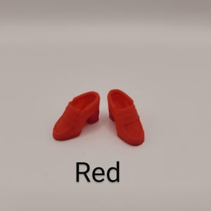 May include: A pair of miniature red loafers with a slip-on design, a rounded toe, and a small block heel. The shoes feature a classic penny loafer strap across the vamp. The word Red is printed in black text below the shoes on a white background.