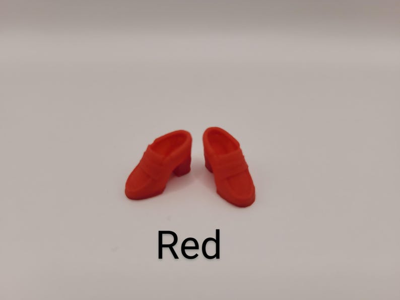 May include: A pair of miniature red loafers with a slip-on design, a rounded toe, and a small block heel. The shoes feature a classic penny loafer strap across the vamp. The word Red is printed in black text below the shoes on a white background.