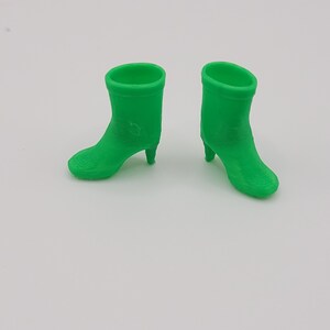Puede incluir: Dos botines verdes brillantes con tacones peque&ntilde;os se muestran sobre un fondo blanco. Los botines tienen una textura suave y un dise&ntilde;o de punta redondeada. Los tacones son delgados y puntiagudos.