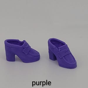 May include: A pair of miniature purple loafers with block heels and a classic penny slot detail across the top. The shoes are solid purple in colour and feature a rounded toe design. The word purple is printed in black text below the shoes.
