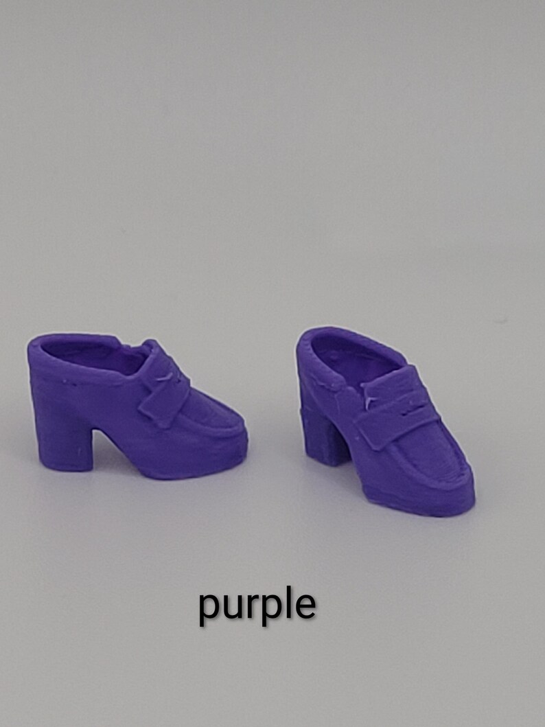 May include: A pair of miniature purple loafers with block heels and a classic penny slot detail across the top. The shoes are solid purple in colour and feature a rounded toe design. The word purple is printed in black text below the shoes.
