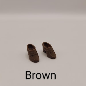 May include: A pair of brown loafers with a block heel and a strap across the vamp. The shoes feature a rounded toe and a smooth finish. The word Brown is printed in black text below the shoes on a plain, light-coloured background.