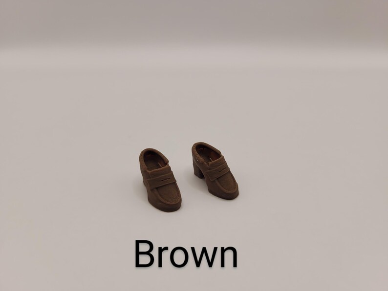 May include: A pair of brown loafers with a block heel and a strap across the vamp. The shoes feature a rounded toe and a smooth finish. The word Brown is printed in black text below the shoes on a plain, light-coloured background.
