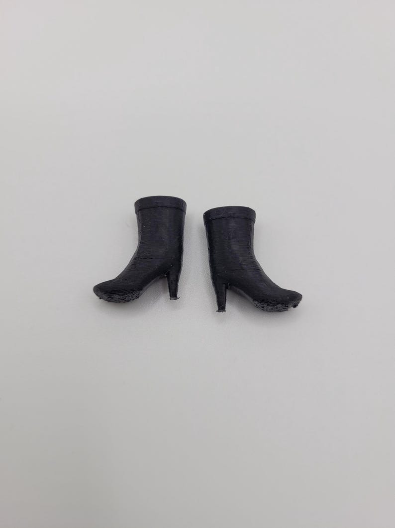 Puede incluir: Un par de botines negros con tacones de aguja. Las botas est&aacute;n hechas de un material texturizado y tienen una punta redondeada. Los tacones miden aproximadamente 5 cm de alto. Las botas est&aacute;n sobre un fondo blanco liso.
