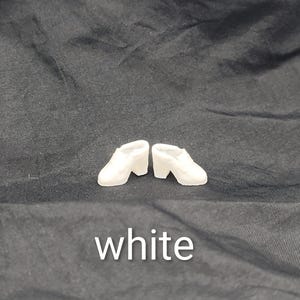 May include: A pair of miniature white shoes with a block heel and a closed-toe design. The shoes are positioned side-by-side. The word white is printed in white text at the bottom of the image, centred below the shoes.