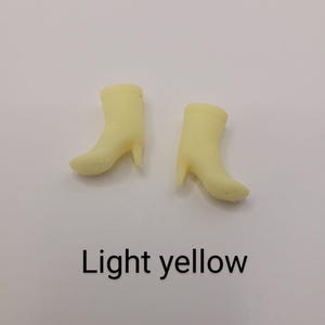 Puede incluir: Dos botas en miniatura de color amarillo claro con tacones se muestran sobre un fondo blanco. El texto "Light yellow" est&aacute; impreso debajo de las botas. Las botas son de color s&oacute;lido y tienen un dise&ntilde;o cl&aacute;sico de bot&iacute;n.